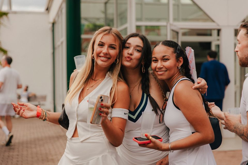 Drei Frauen in weißen Tennis-Outfits lachen in die Kamera